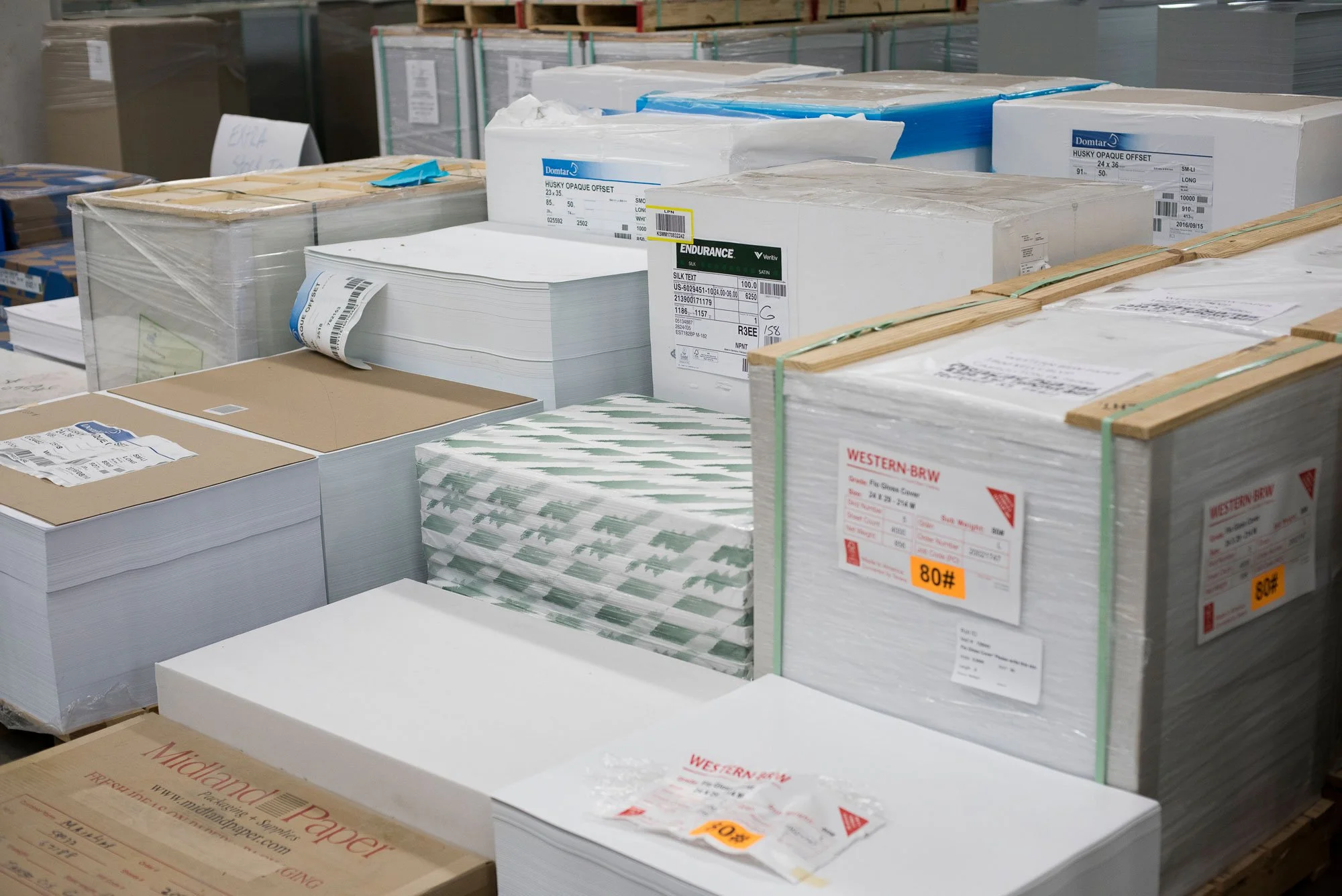 Stacks of paper reams and boxes of paper on pallets in a warehouse.
