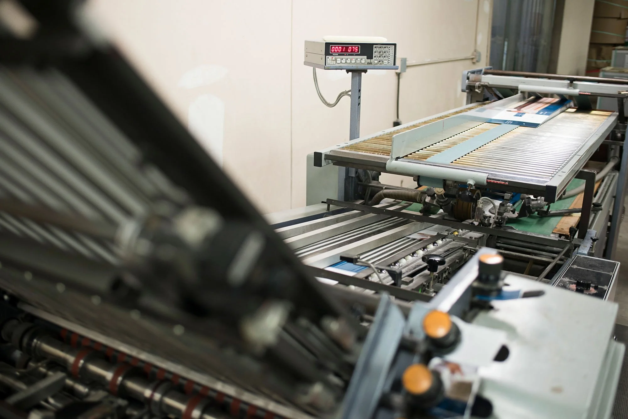 Industrial printing or packaging machinery in a factory setting with a digital control panel and conveyor system.