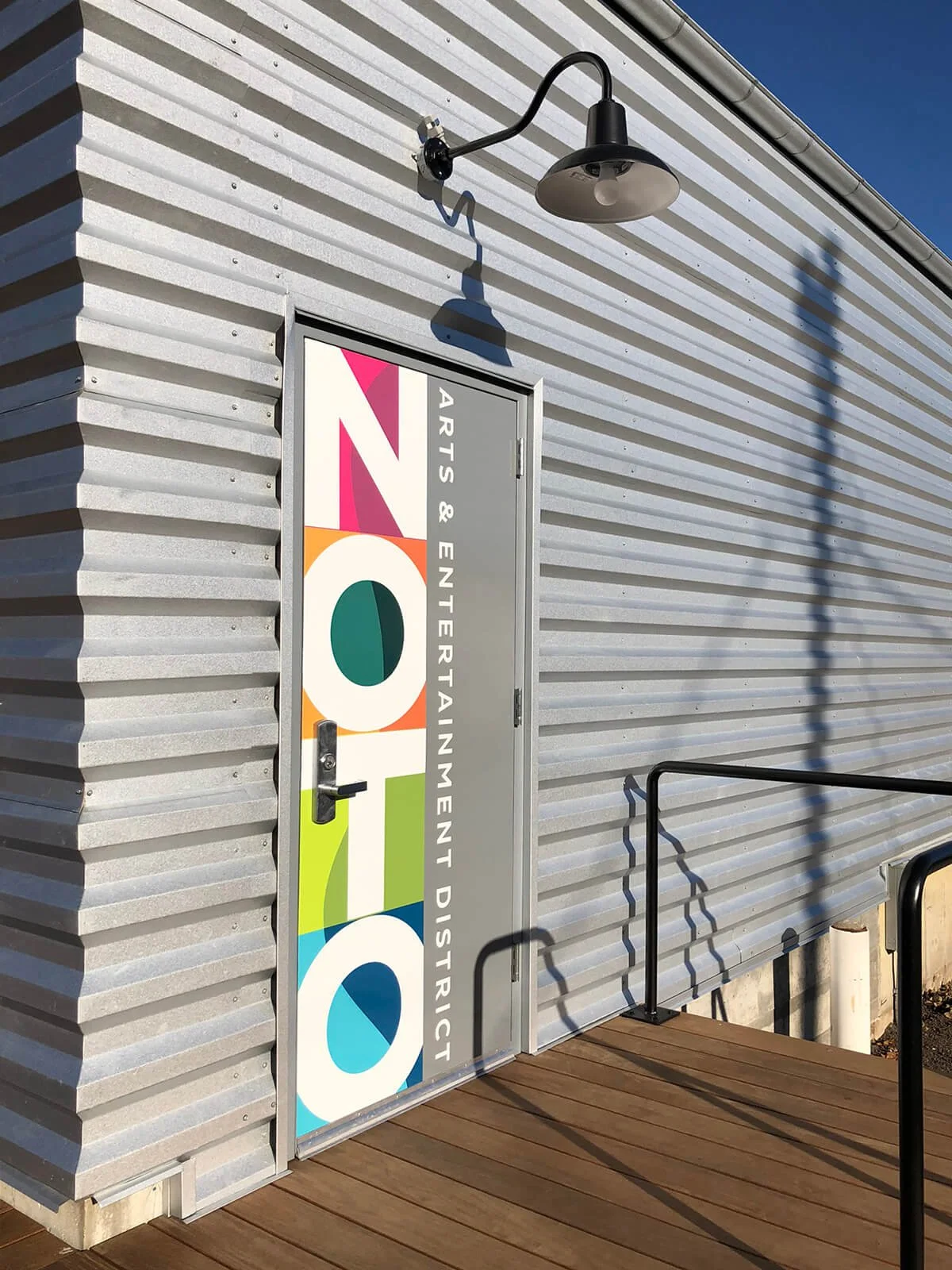 Door with colorful artwork and text for Arts & Entertainment District on a building exterior, with black wall-mounted light fixture and railings.