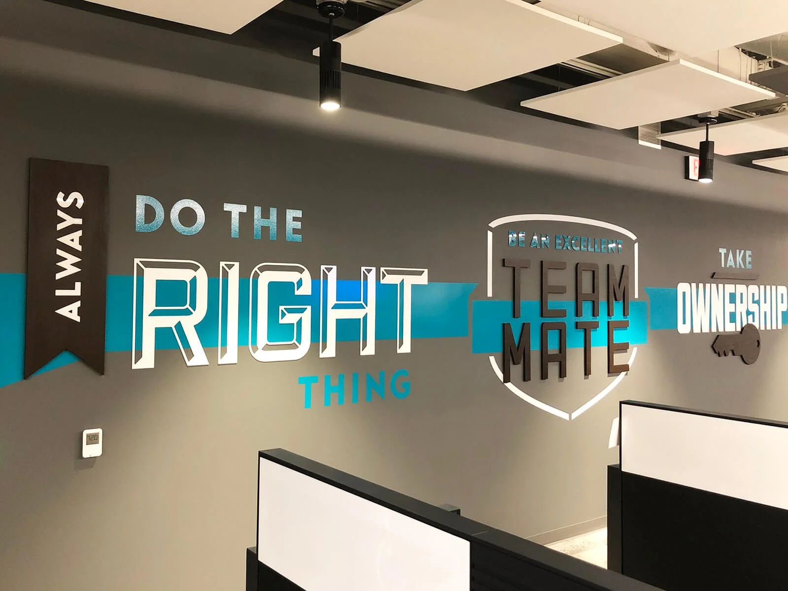 Decorative wall with motivational team-building quote in a modern office. The quote says 'Always do the right thing, be an excellent team mate, and take ownership.' It features various fonts, colors, and a key graphic.