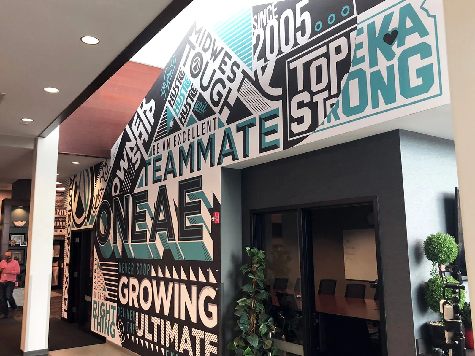 Congregation wall with motivational words and phrases including "Be an excellent teammate," "One as never stop growing," and "Top ranking," in a modern office setting. Small plants are visible near the window.