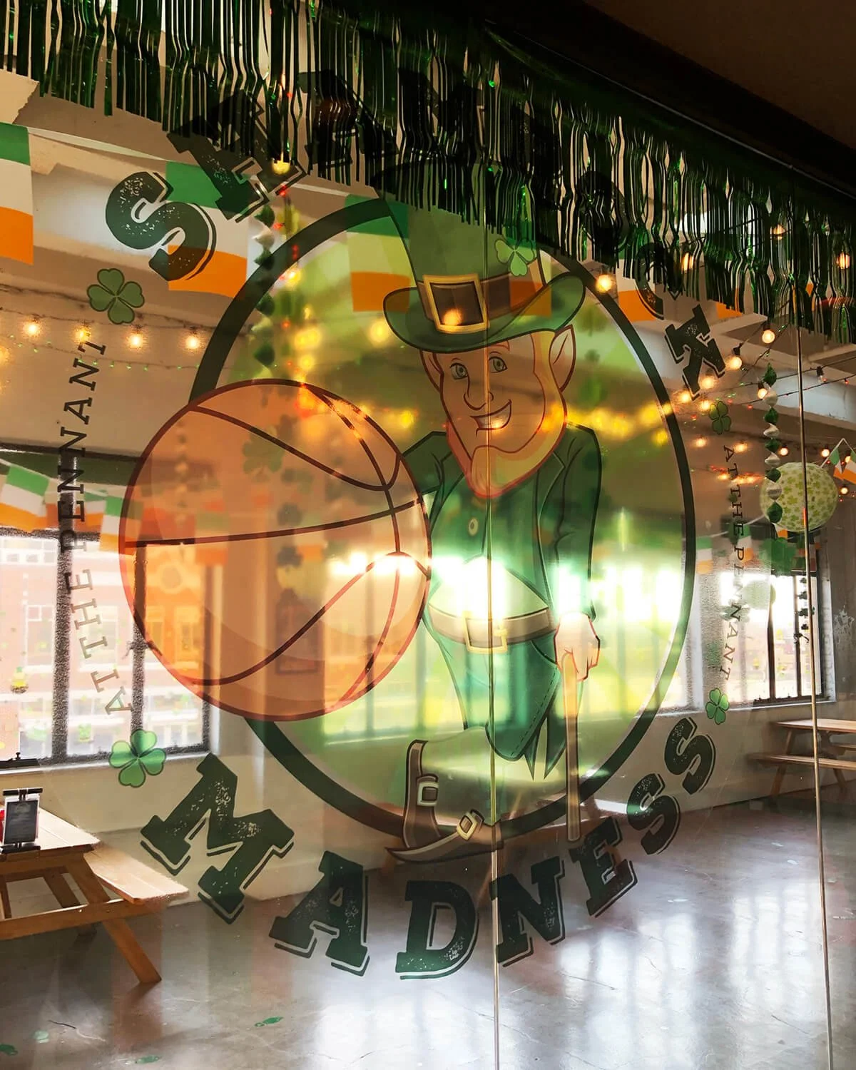Decorative window with a St. Patrick's Day theme, featuring a leprechaun with a hat, holding a basketball, and shamrock and rainbow decorations.