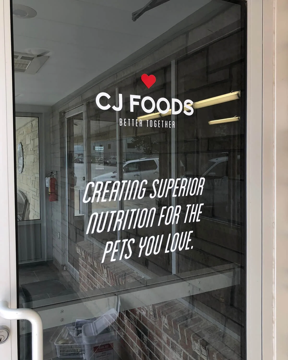 Glass door with CJ FOODS logo, tagline 'Better Together', and the message 'Creating superior nutrition for the pets you love'.