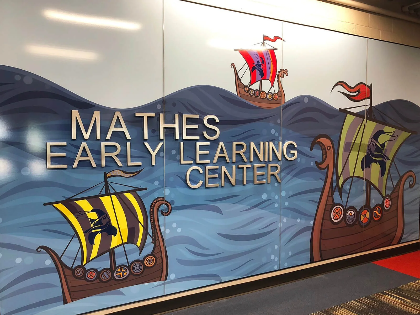 Decorative wall mural showing Viking ships sailing on stylized blue waves, with the words 'Mathes Early Learning Center' displayed prominently.