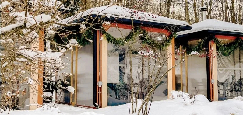 A small building or shed with glass windows, surrounded by snow and trees, decorated with green holiday garlands.  The Riverbend Condos, Huntsville, Muskoka.