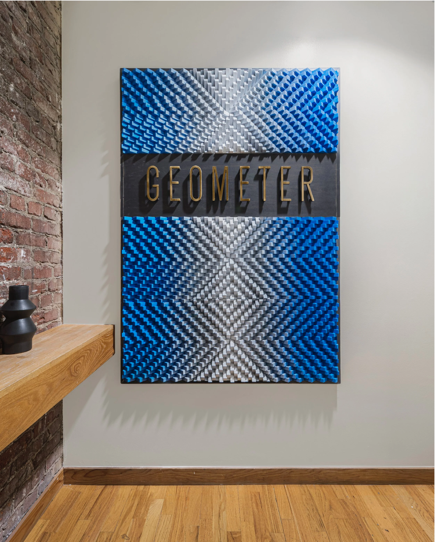 Geometer office feature wall with custom geometric art in textured blue and silver, finished with gold GEOMETER lettering, creating a bold branded focal point in a modern tech workplace.