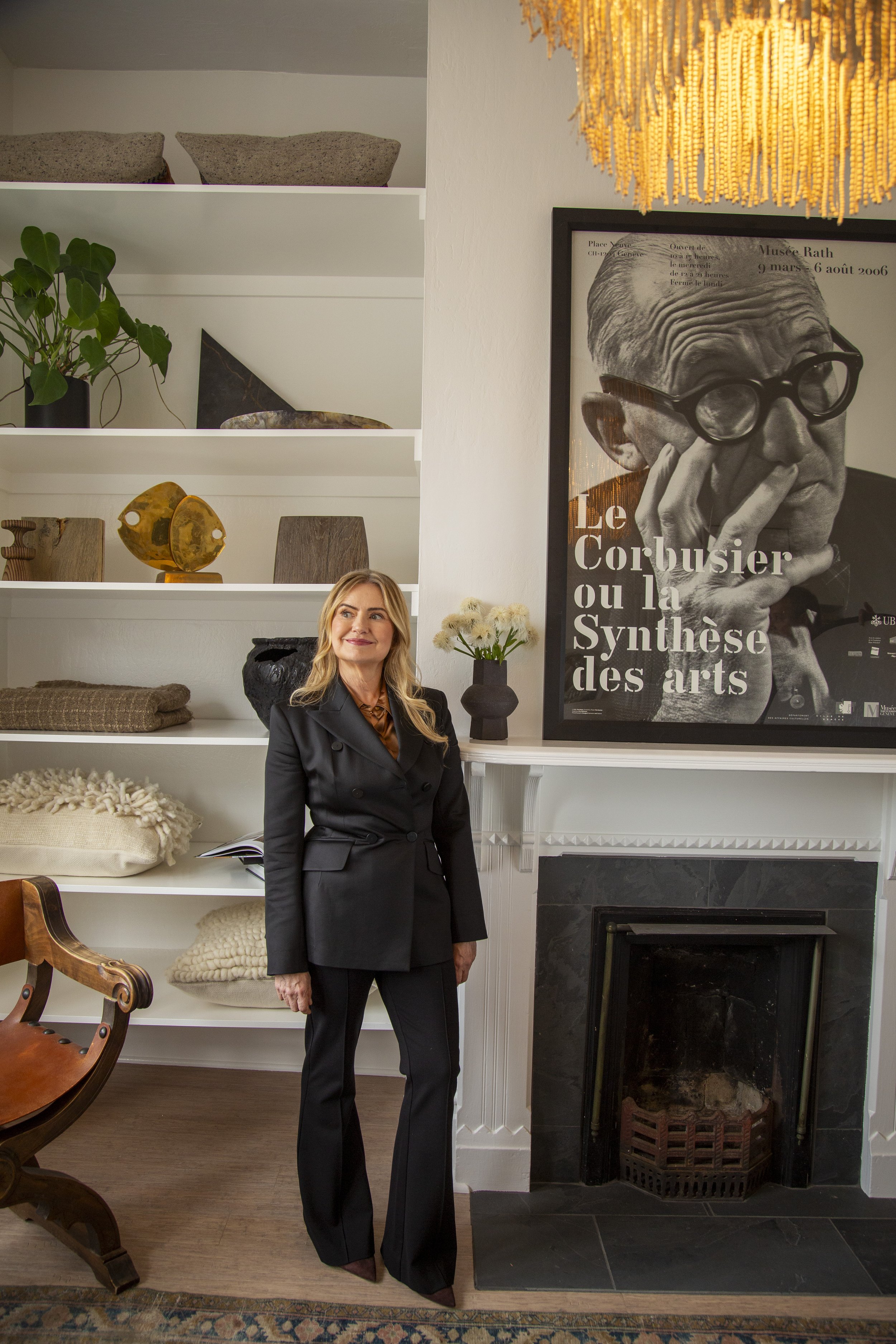 Sabra Ballon stands beside a modern fireplace in a refined living room with white built in shelves and a large black and white portrait, reflecting ballonSTUDIO’s calm luxury interior design approach in San Francisco.