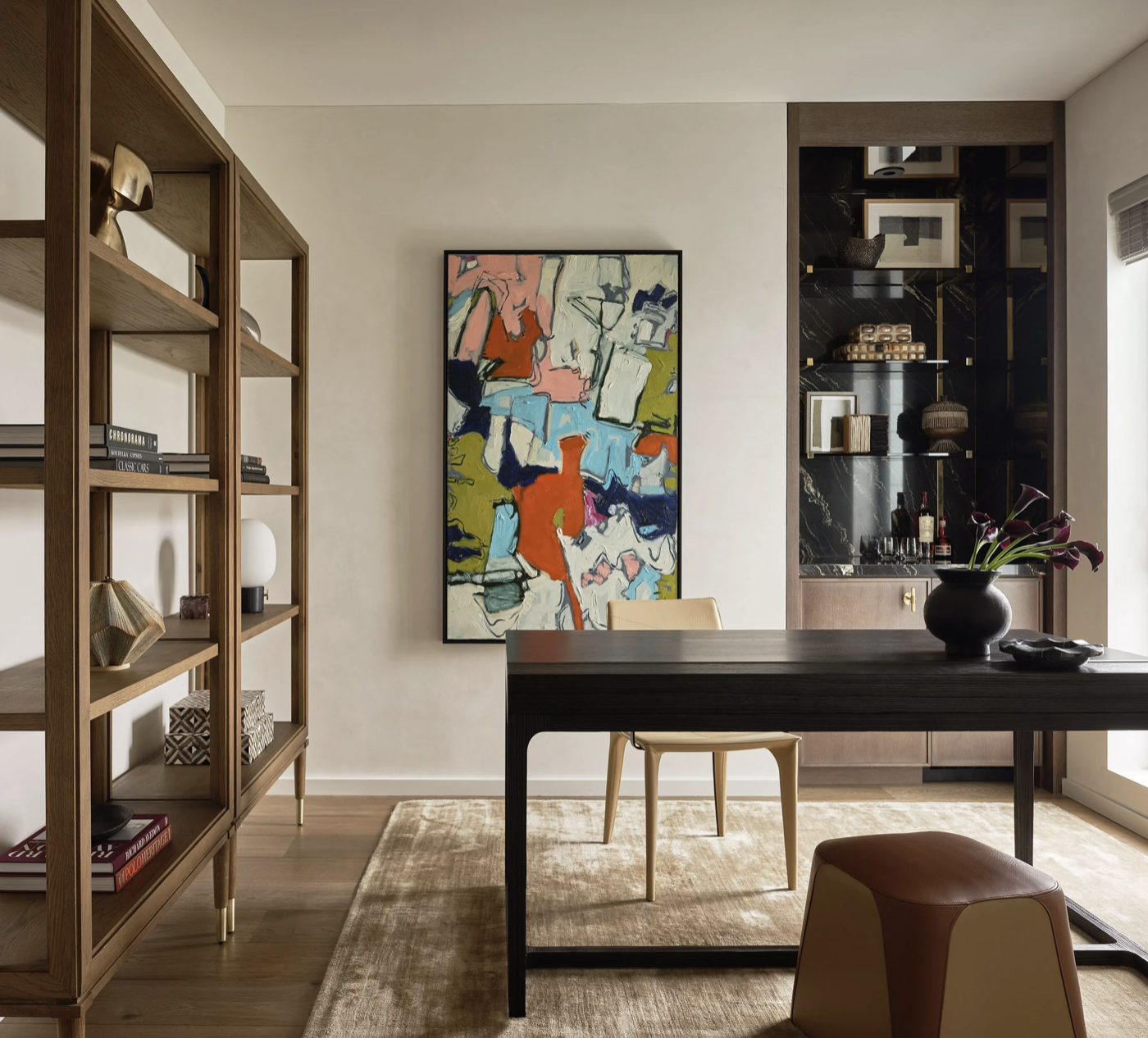 Home office with black desk, built in shelving, colorful abstract art, and bar niche in dark stone, styled for modern San Francisco penthouse living.