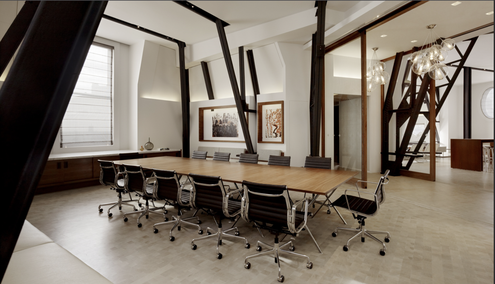 Kearny One historic San Francisco conference room with a large wood table and black leather rolling chairs, framed by geometric steel beams, contemporary glass chandeliers, and curated artwork for a refined modern workplace.