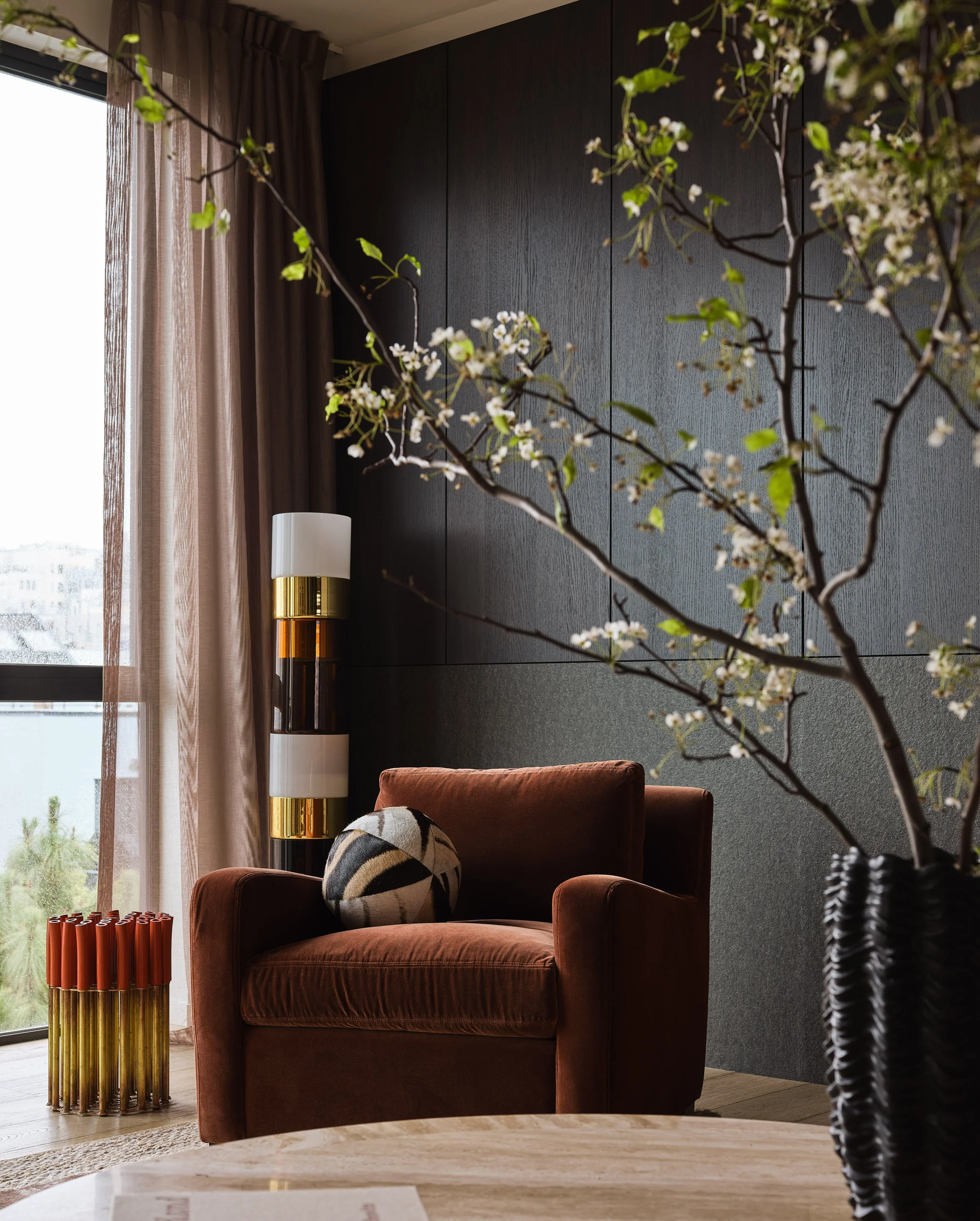 Broadway Penthouse Pacific Heights living room vignette with a rust lounge chair, sculptural lamp, and flowering branches beside large windows and soft drapery, capturing calm modern luxury interior design in San Francisco.