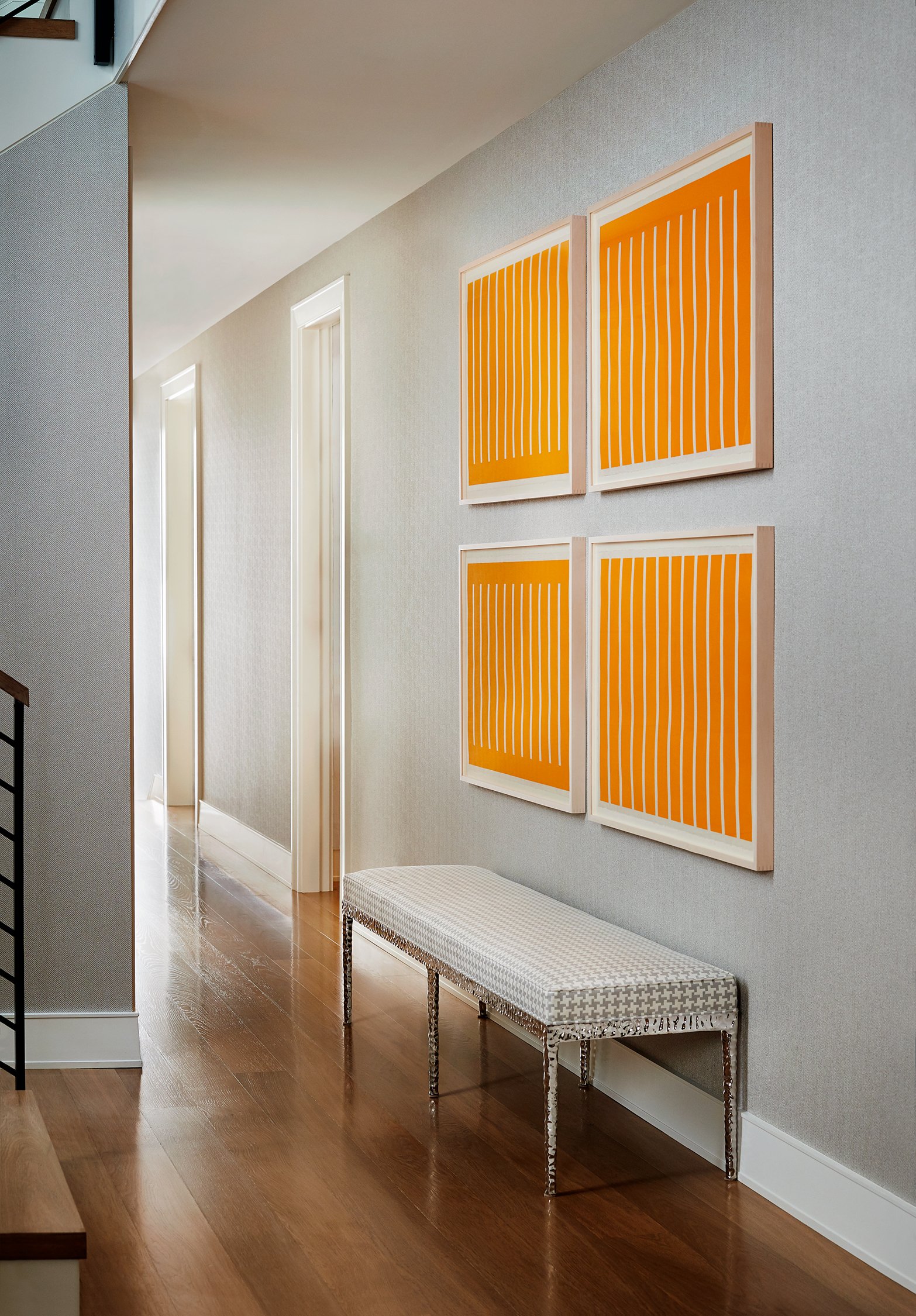 Filbert Street Pacific Heights in San Francisco this hallway with four orange abstract artwork pieces on the wall, a patterned bench, and natural light coming through narrow windows.