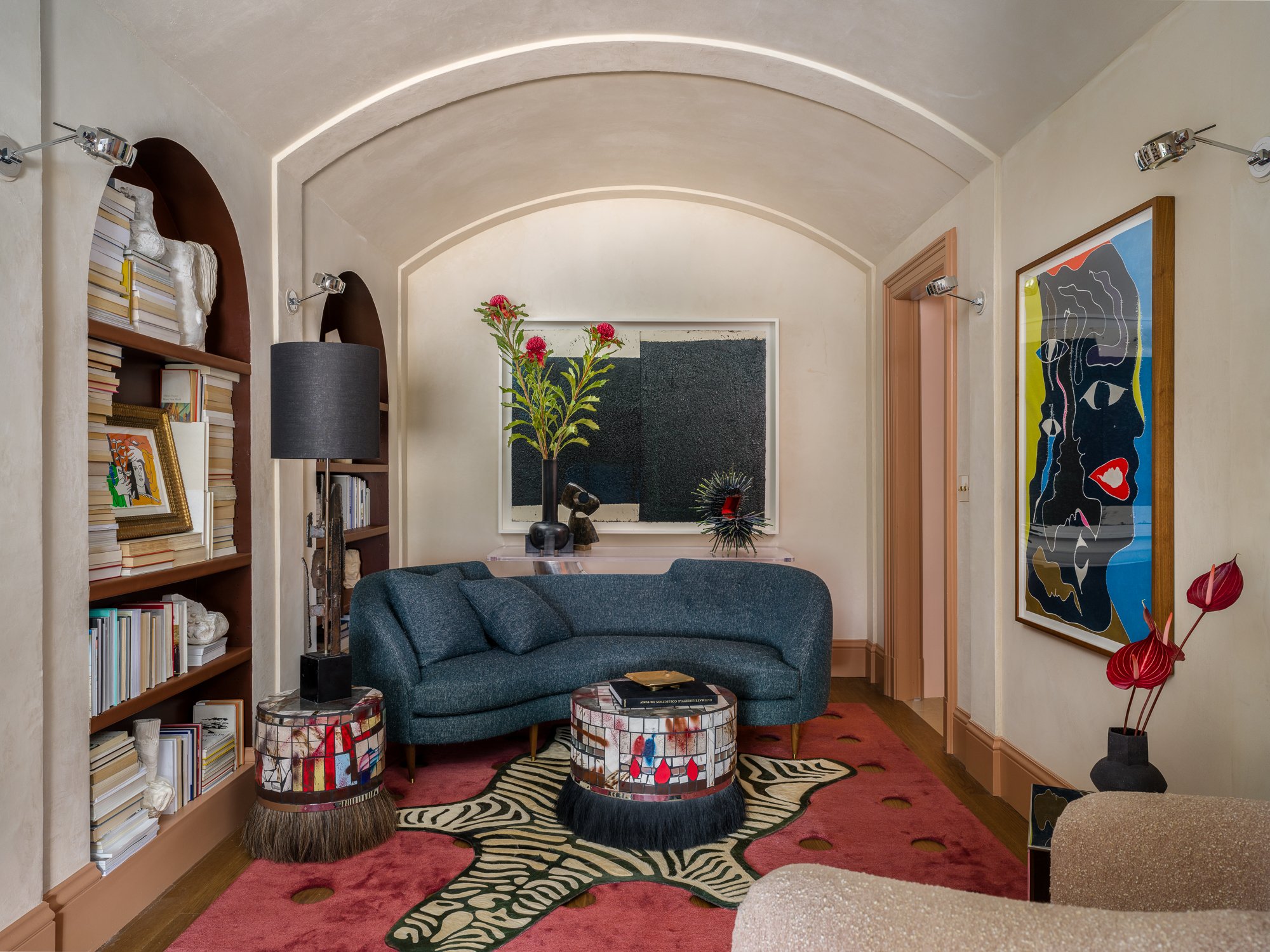 San Francisco Decorator Showcase 2024 living room with a blue sofa, patterned stools, and colorful art, styled with books on built in shelves and leafy plants for an art forward, collected interior.