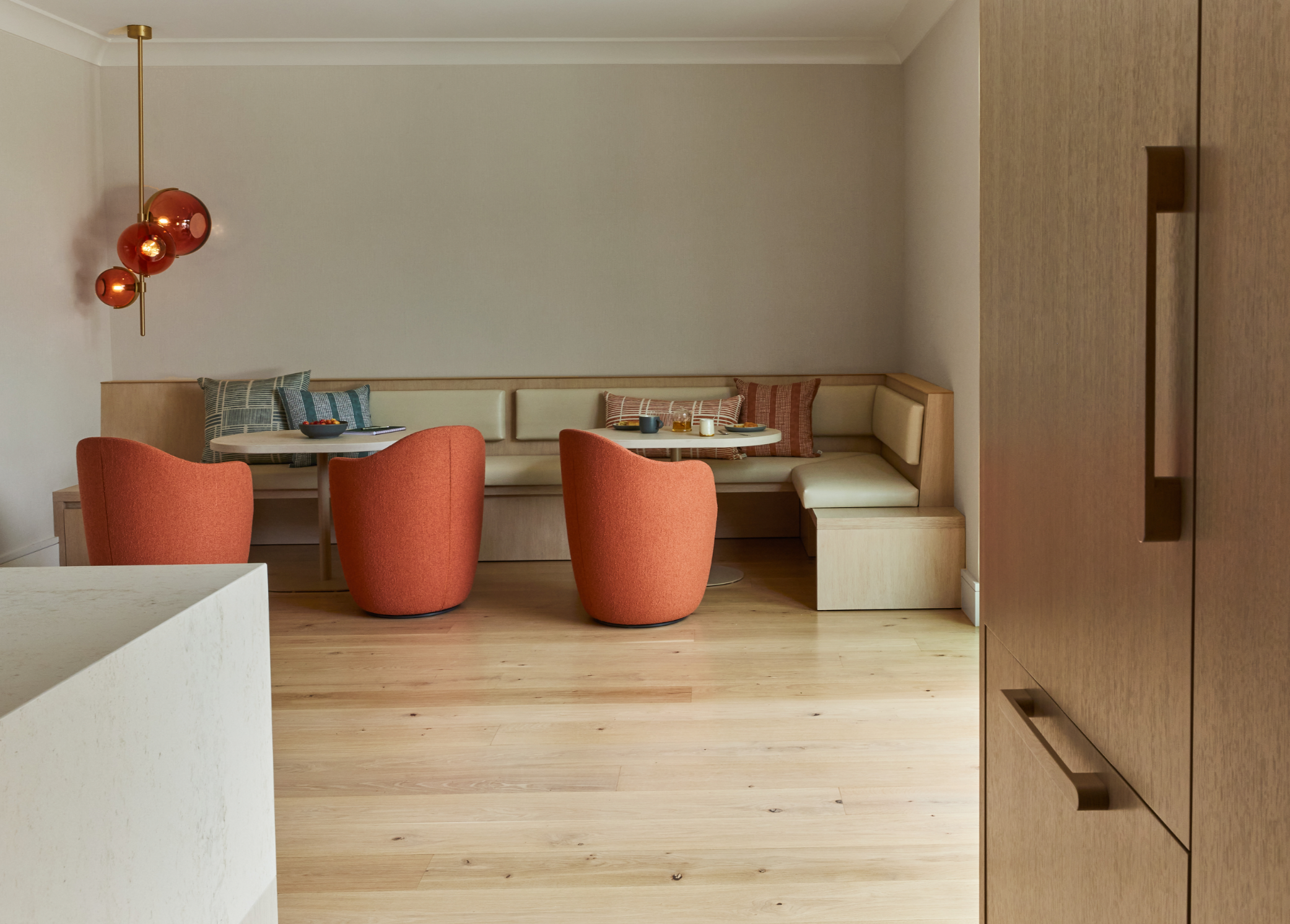 Union Street Marina District dining nook in San Francisco with upholstered corner banquette, two orange armchairs, and a round table under a modern pendant, set within warm wood floors and cabinetry for modern luxury interior design.