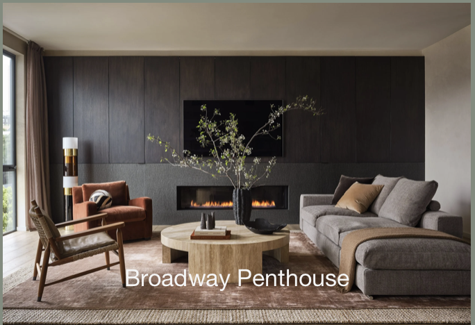 Living room with a fireplace, a large gray sofa, a wooden armchair, a round coffee table with decor, and a large window with curtains in a Broadway penthouse. BallonStudio led by Sabra Ballon is one of the best luxury interior designers in San Fran