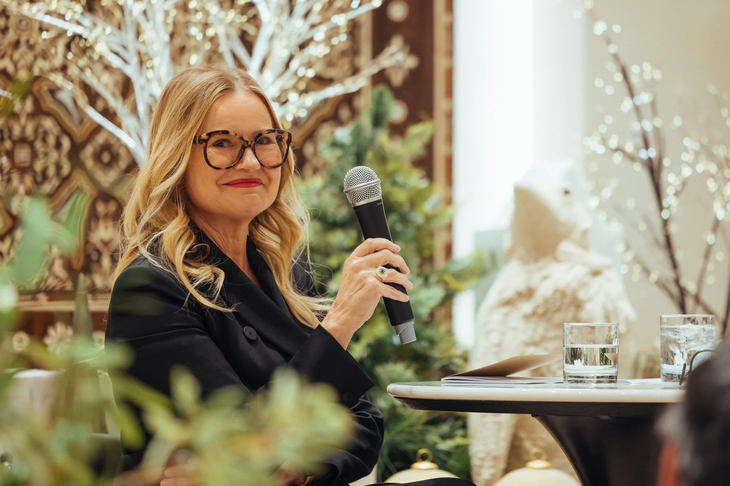 Sabra Ballon speaks at a holiday design gathering, holding a microphone and smiling in front of Christmas decor, reflecting ballonSTUDIO’s San Francisco interior design leadership and community presence.