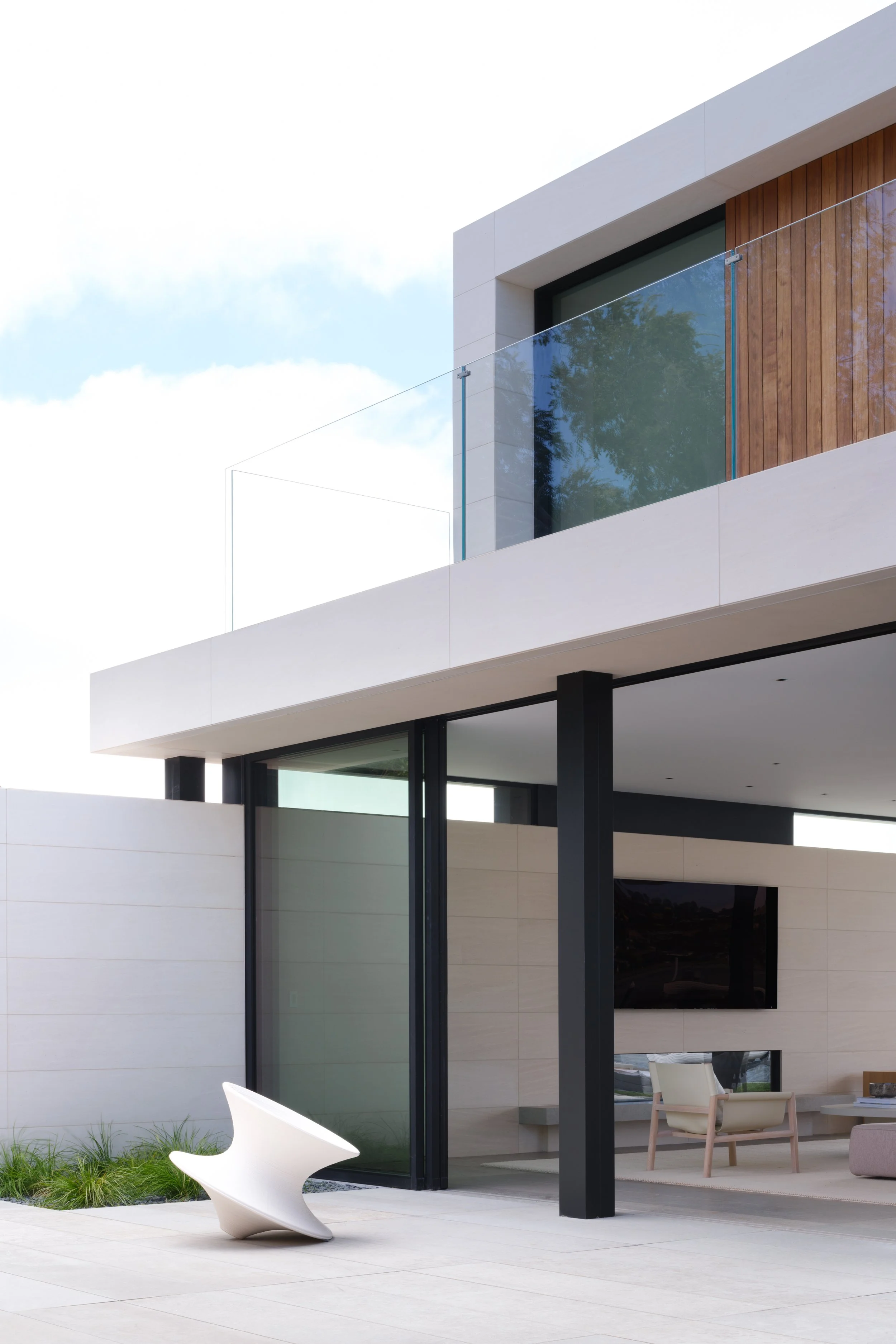 Modern Tiburon waterfront home with large glass doors and white exterior walls, featuring a patio seating area with a sculptural white chair that supports indoor outdoor living and modern Marin County coastal design.