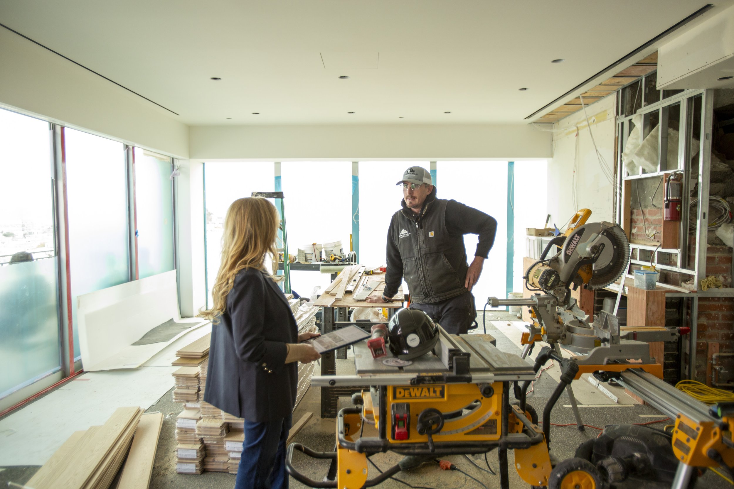 Sabra Ballon, Interior designer reviews plans with a contractor in a bright renovation space, surrounded by tools and lumber, coordinating build details for a custom residential project.