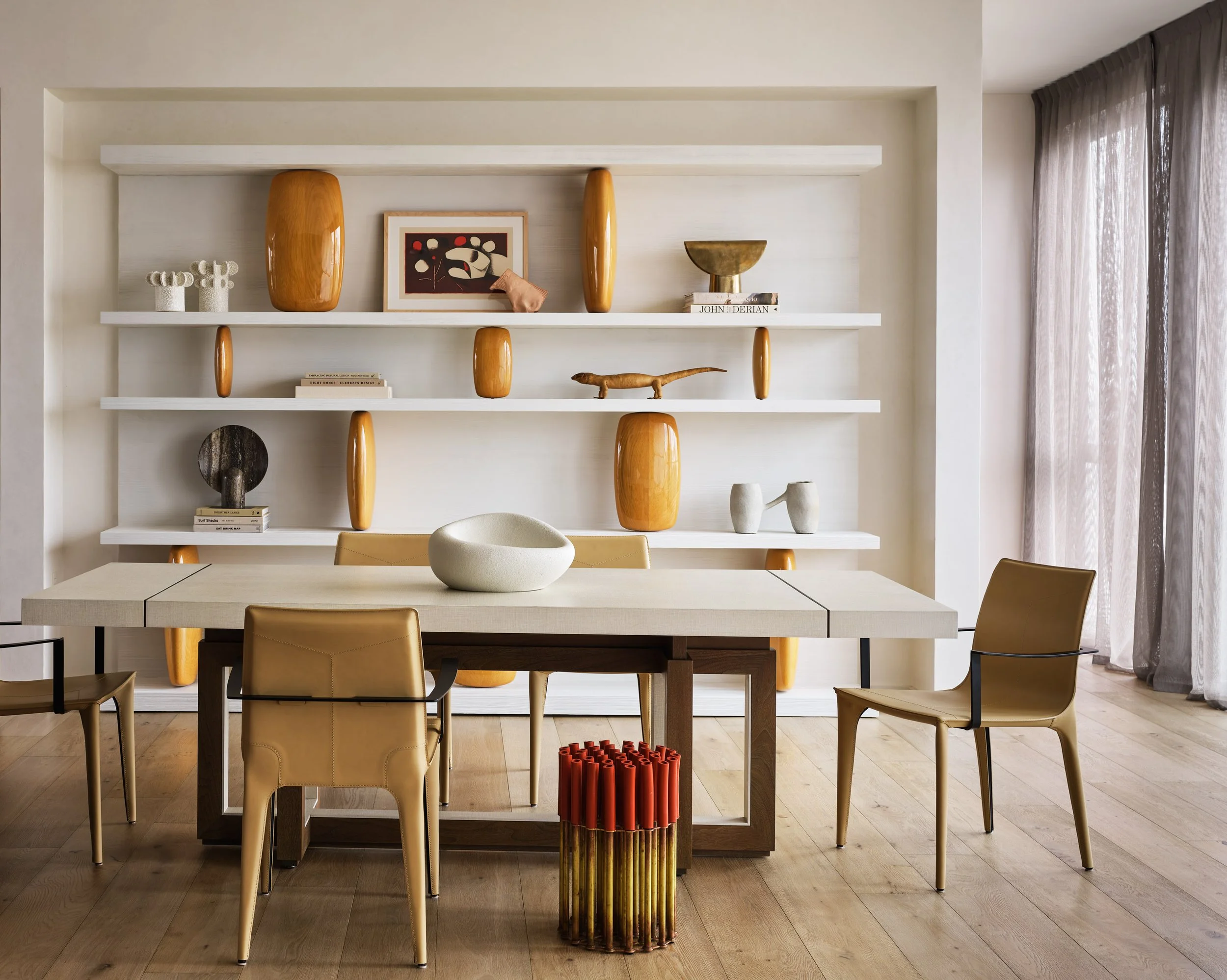 Broadway Penthouse Pacific Heights dining area with a beige table and tan chairs, styled with a white bowl and built in shelves of art and vases, framed by sheer curtains for calm modern luxury in San Francisco.