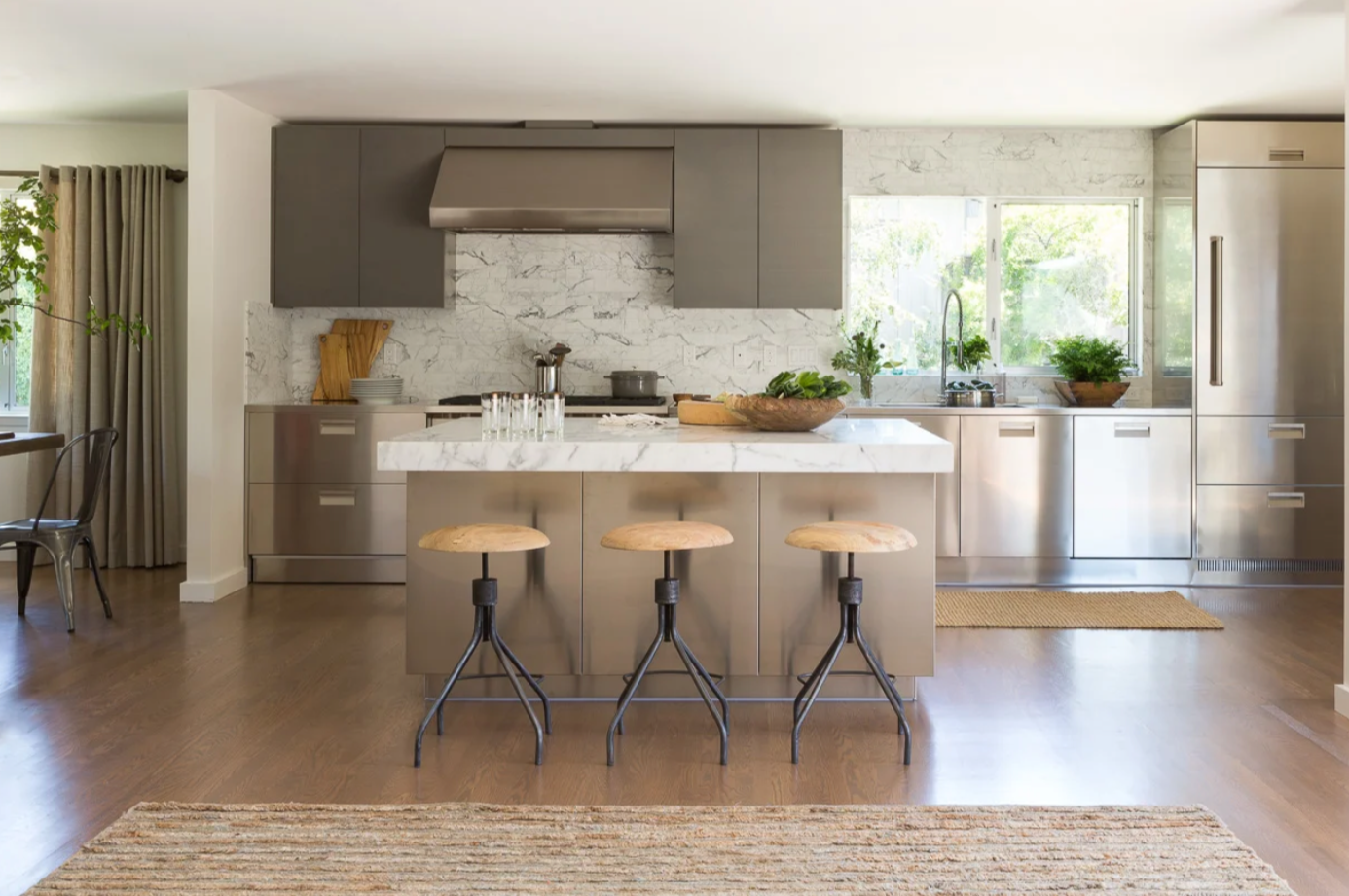 Modern kitchen with white marble countertops, gray cabinets, stainless steel appliances, window with greenery outside, and wooden bar stools on the Penisula in South Bay.