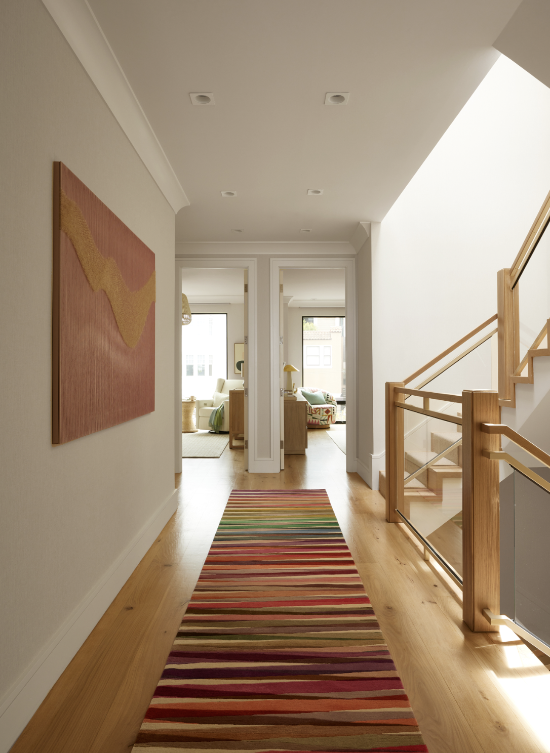 Union Street Marina District hallway in San Francisco with warm wood floors, a striped runner, and colorful art, connecting light filled living spaces through open doorways for modern luxury residential interior design.