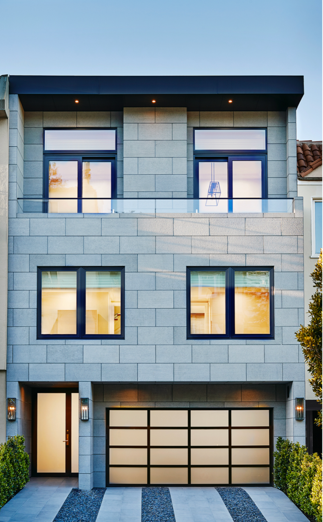 Modern multi-story house with a gray stone exterior, large black-framed windows, a garage with a frosted glass paneled door, and a small front yard with greenery Filbert Street Pacific Heights in San Francisco