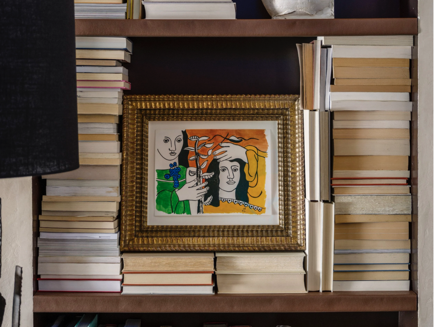 Colorful framed artwork in the style of Pablo Picasso showing abstract faces and a hand, displayed among stacked books on a built in shelf in the 2024 San Francisco Decorator Showcase library.