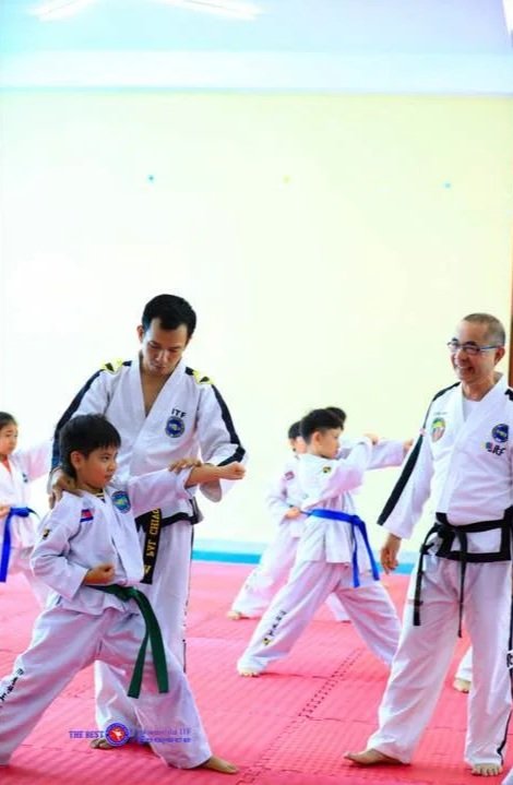 Martial arts class with children and instructors practicing on red mats in a bright room.