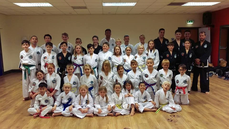 Group of children and adults in martial arts uniforms in a dojo, posing for a photo.