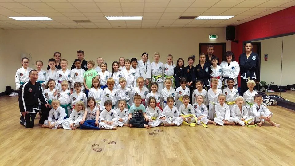 Group of children and adults in martial arts uniforms in a dojo.