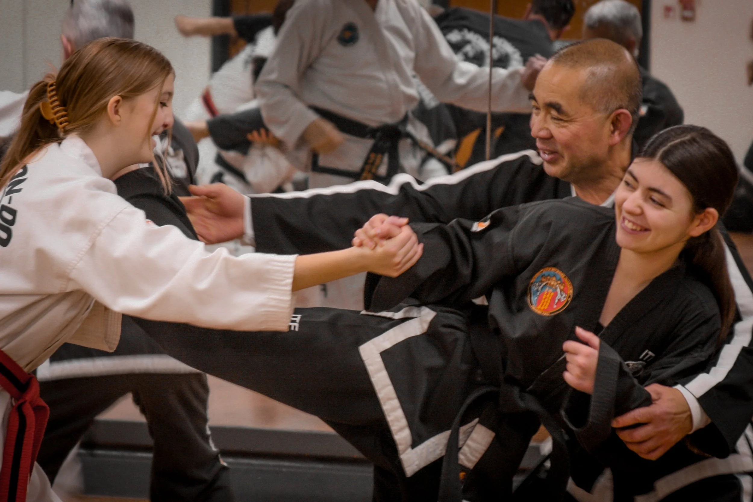Two martial arts students, a young girl and a woman, shaking hands with two instructors in a martial arts class, smiling and exchanging respect.