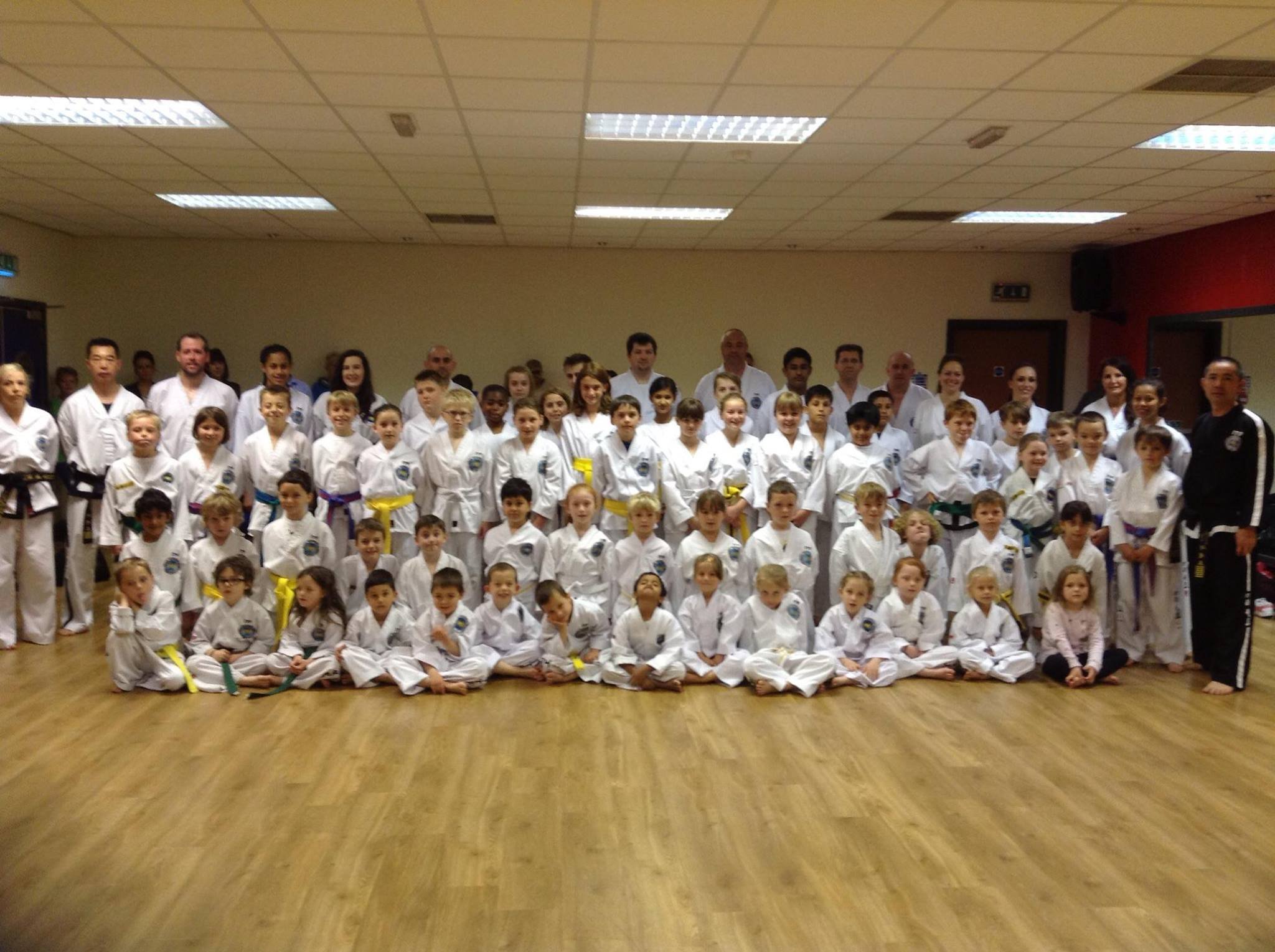 Group photo of children and adults in martial arts uniforms in a training room.