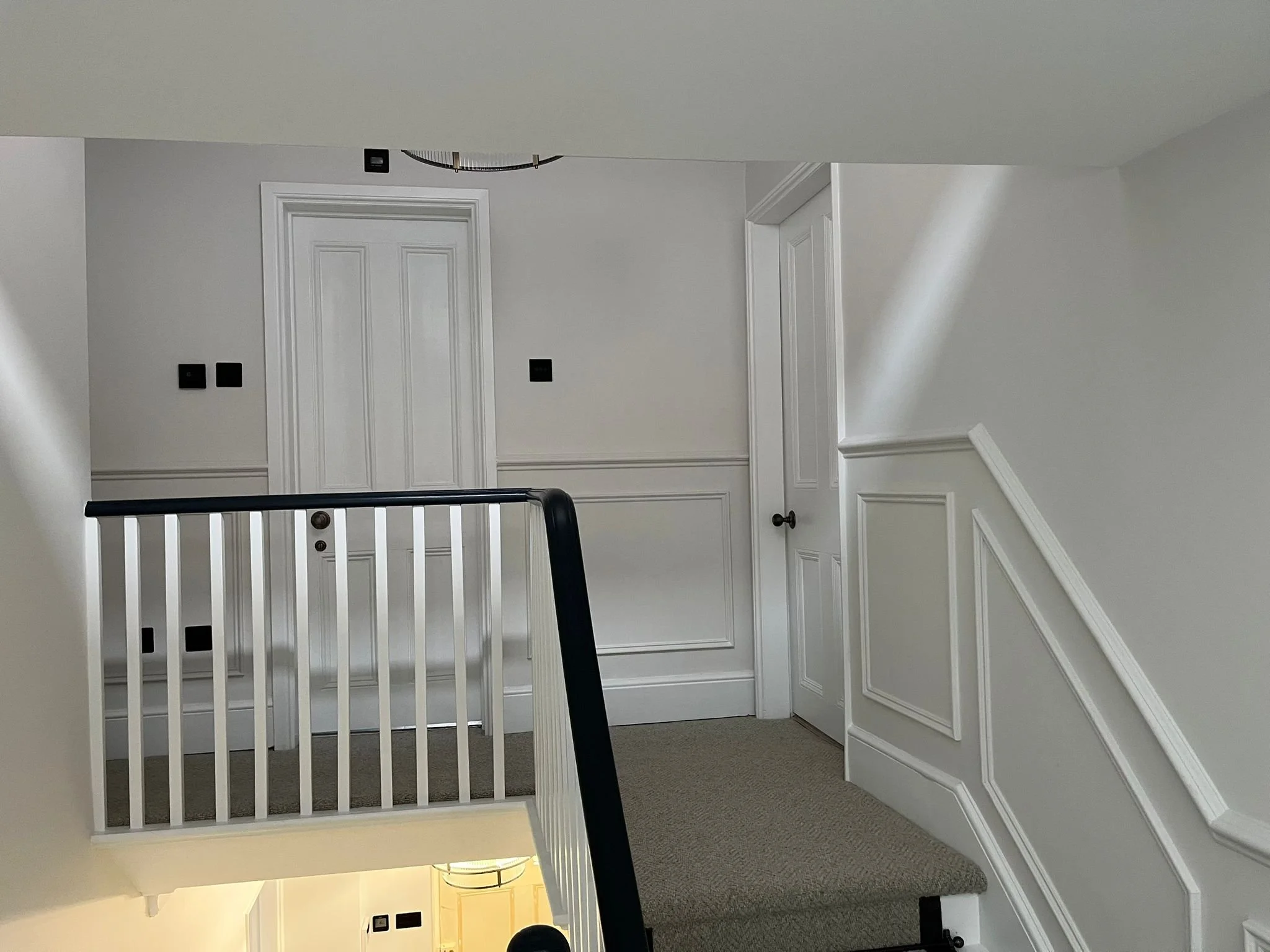 Interior view of a white staircase landing with two white doors, black switches, and a black handrail