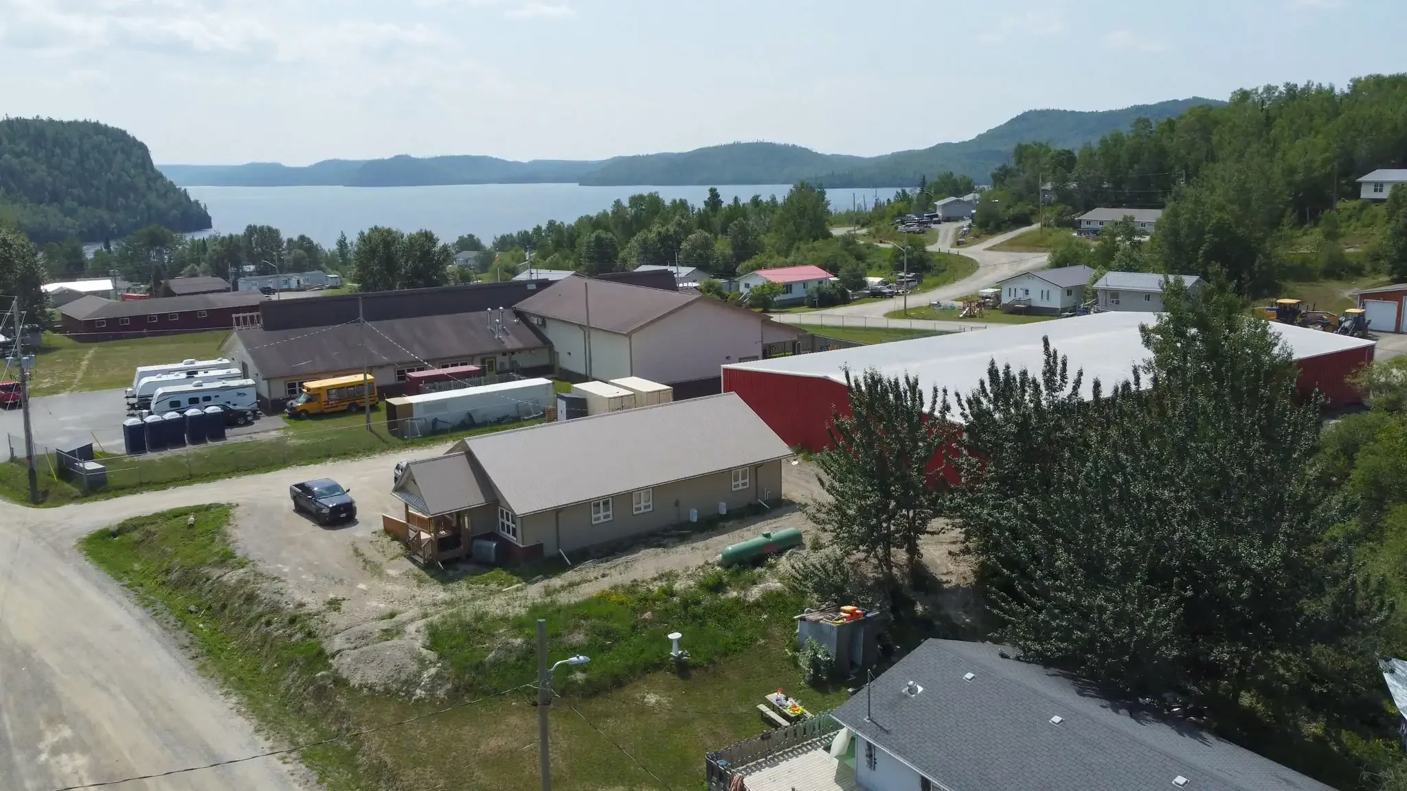 Aerial view of a small lakeside town with houses, commercial buildings, trees, and a large body of water in the background on a clear day.