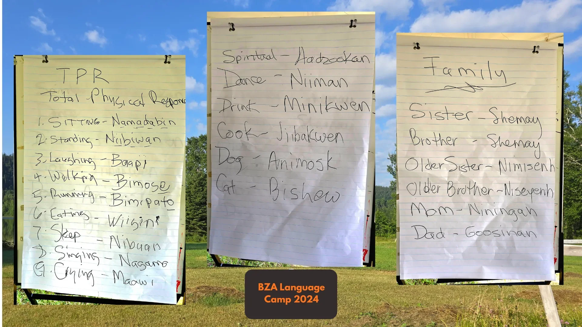 Three large hand-written posters on easels outdoors during daytime, titled 'BZA Language Camp 2024', listing various words and their meanings or relationships, including topics like family, spiritual, and physical responses.