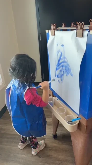 Young girl painting a blue dragon on paper set up on an easel.