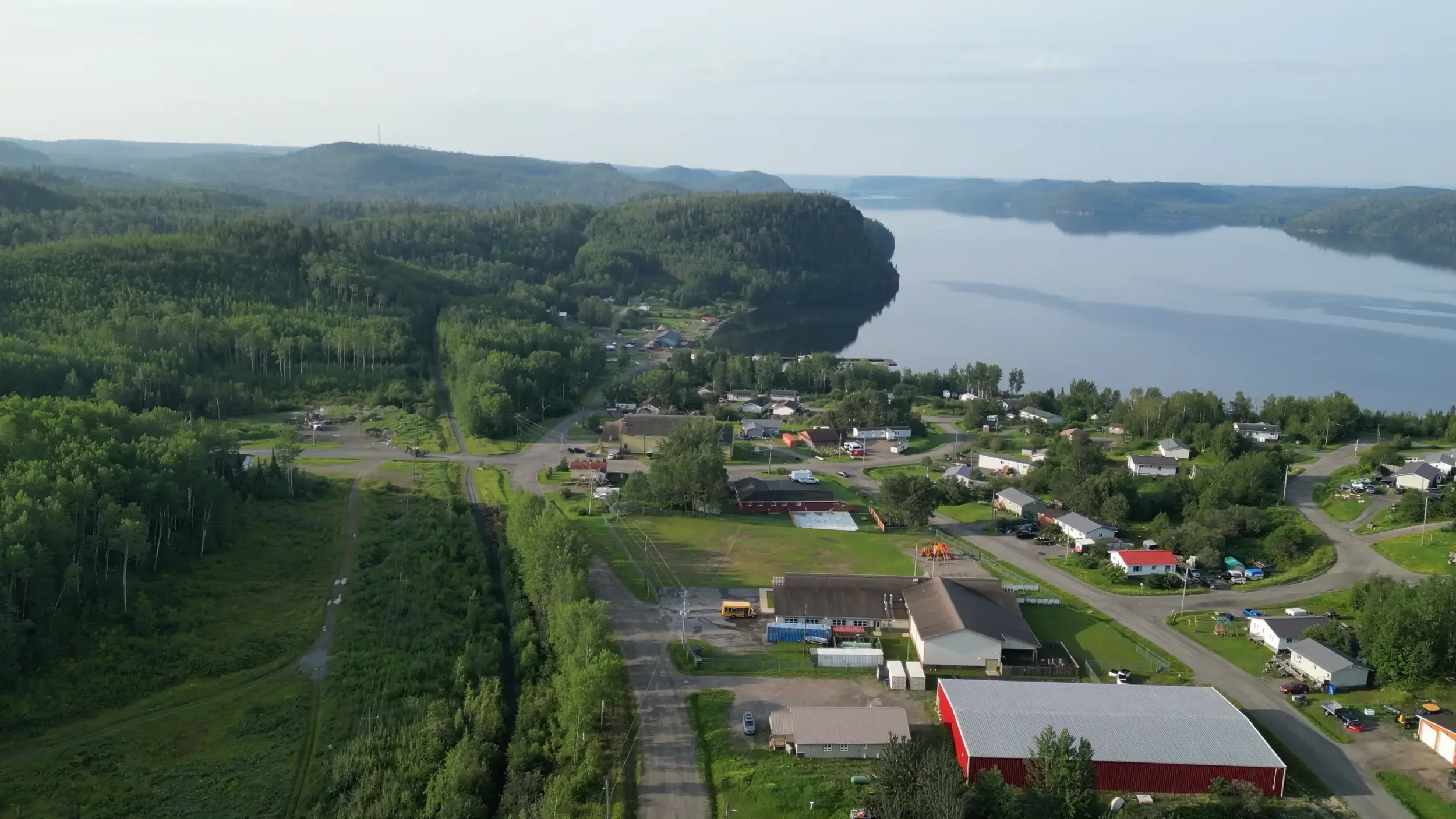 Aerial view of a small town next to a large river, surrounded by lush green forests and hills.