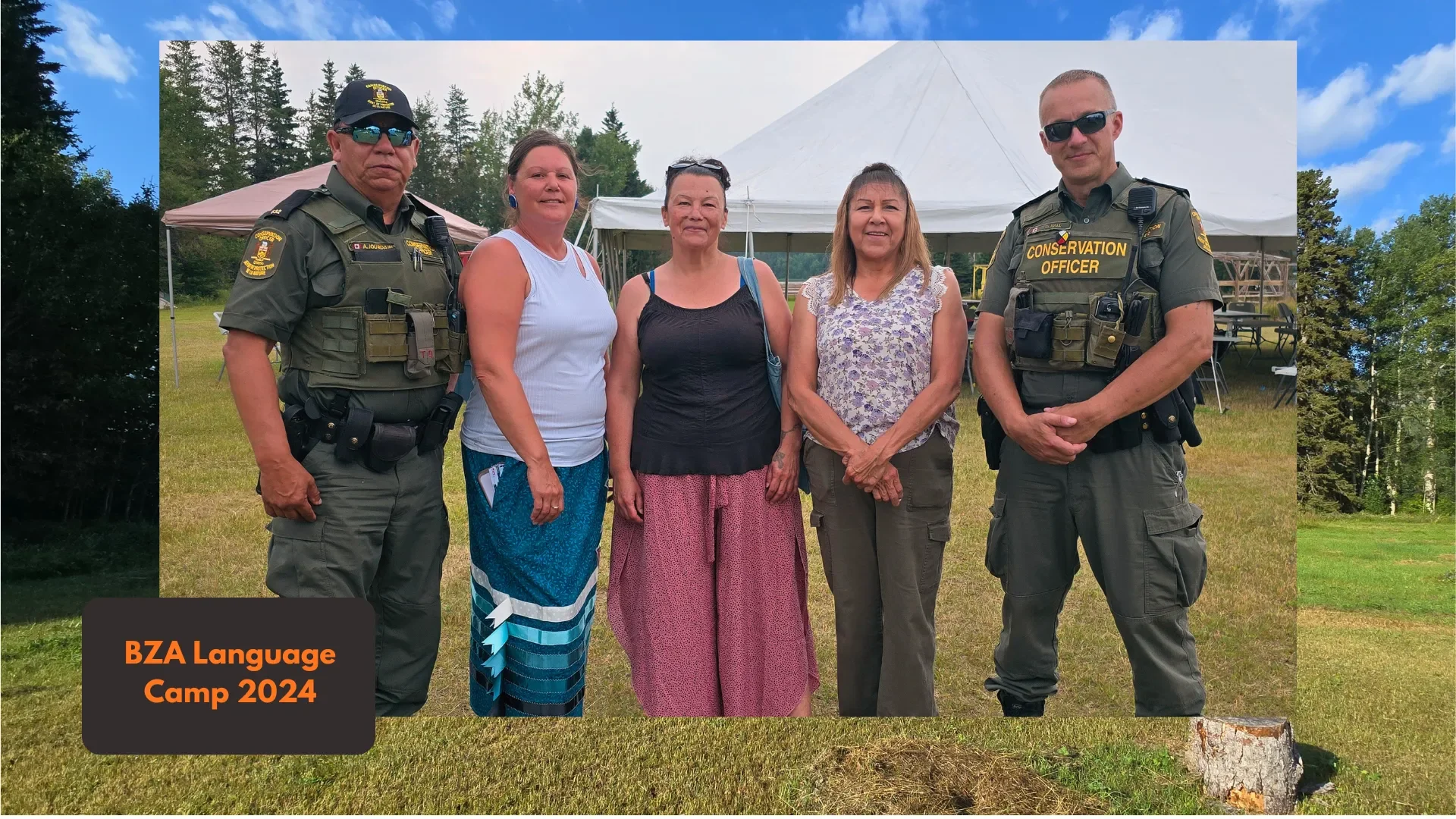 Group of five people standing outdoors in front of a white tent, including two police officers in uniform and three women, at BZA Language Camp 2024.
