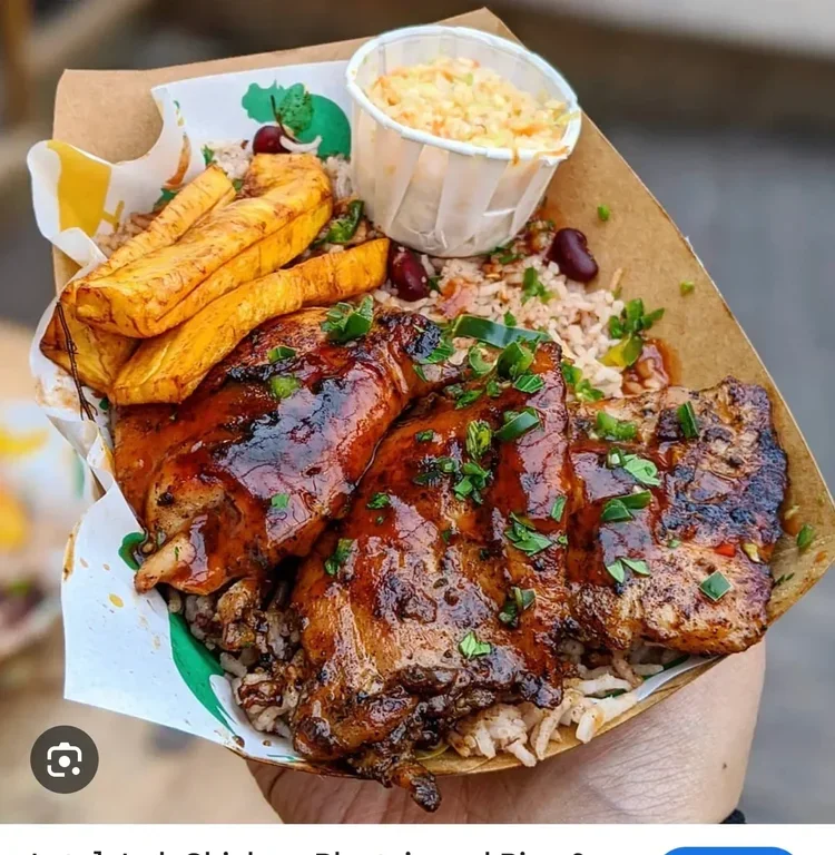 A takeout tray with grilled chicken covered in barbecue sauce, rice, plantains, and a side of coleslaw in a small cup.