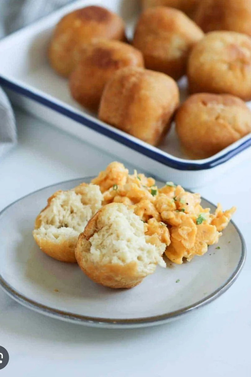 Plate with two half-eaten fried chicken biscuits and a serving of macaroni and cheese, with more fried chicken biscuits in a dish in the background.