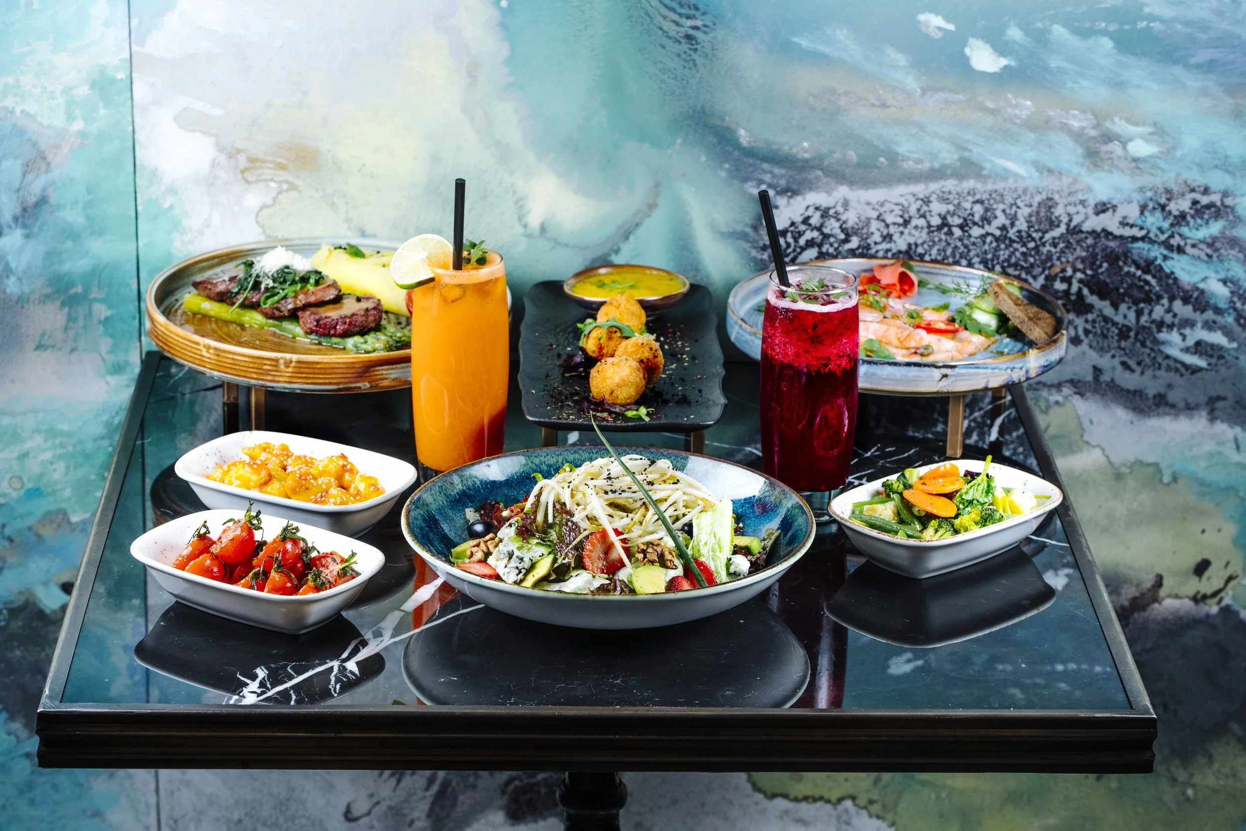 A table with various dishes including salads, fried appetizers, and beverages, set against an ocean-themed background.