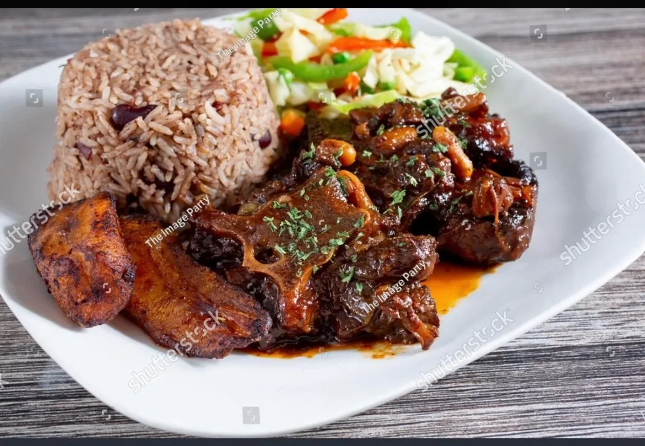 Plate with rice, a meat stew with herbs, a fried plantain, and a vegetable salad on a white plate.