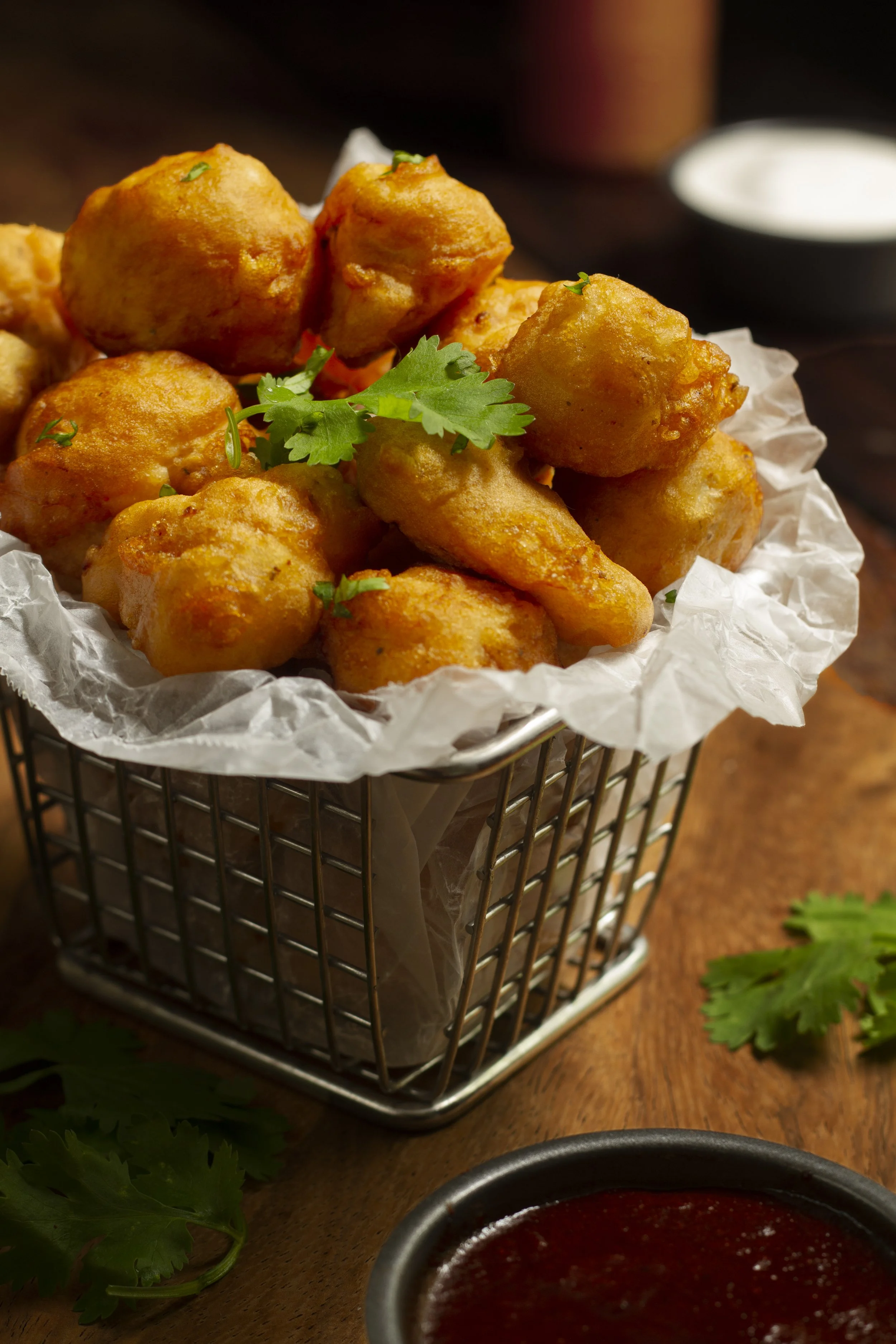 Basket of fried chicken nuggets garnished with cilantro, with dipping sauce in a small bowl nearby.