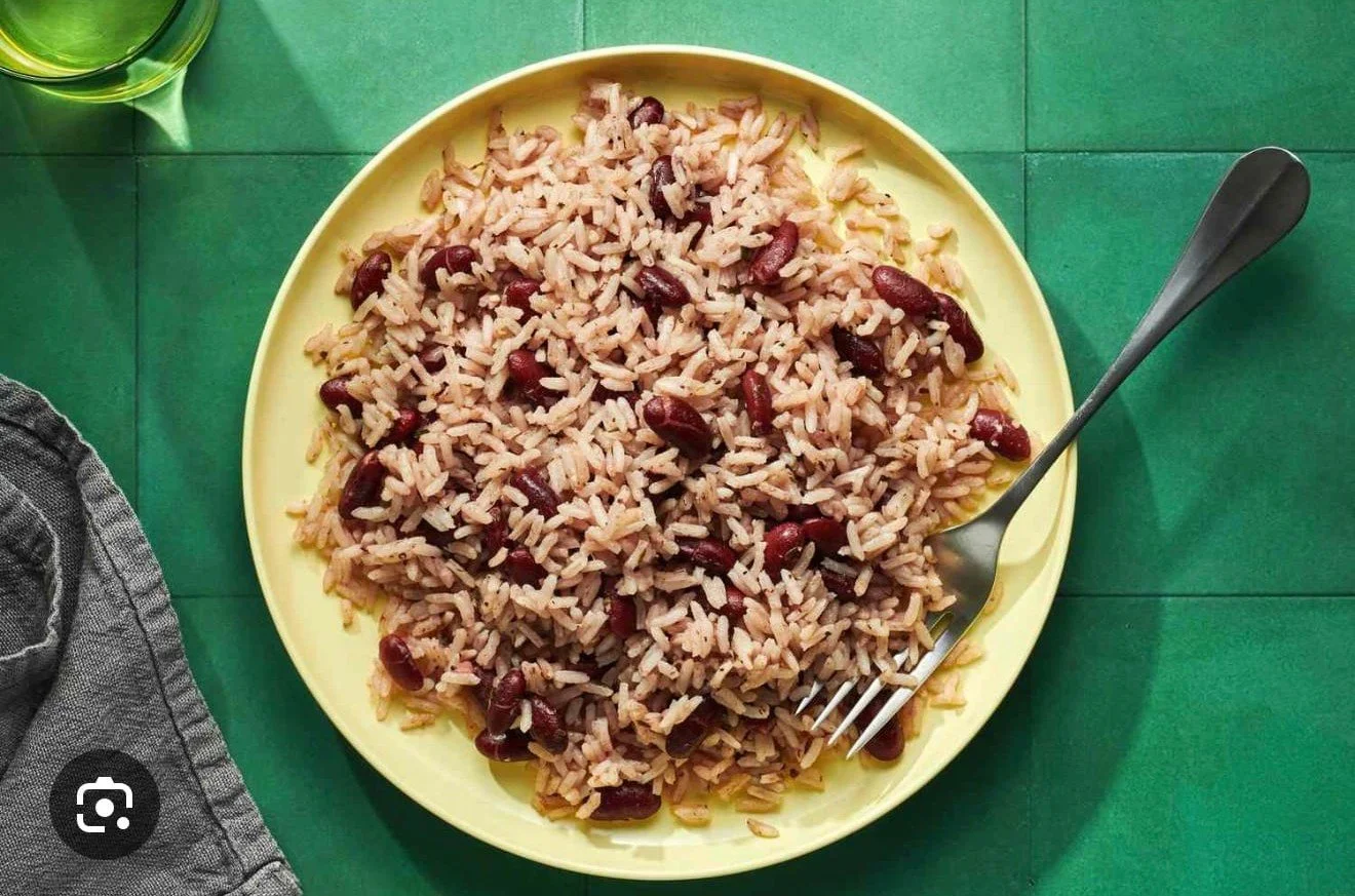 A yellow plate filled with cooked rice and kidney beans, with a fork resting on the right side of the plate, on a green table with a glass of water partially visible at the top left corner.