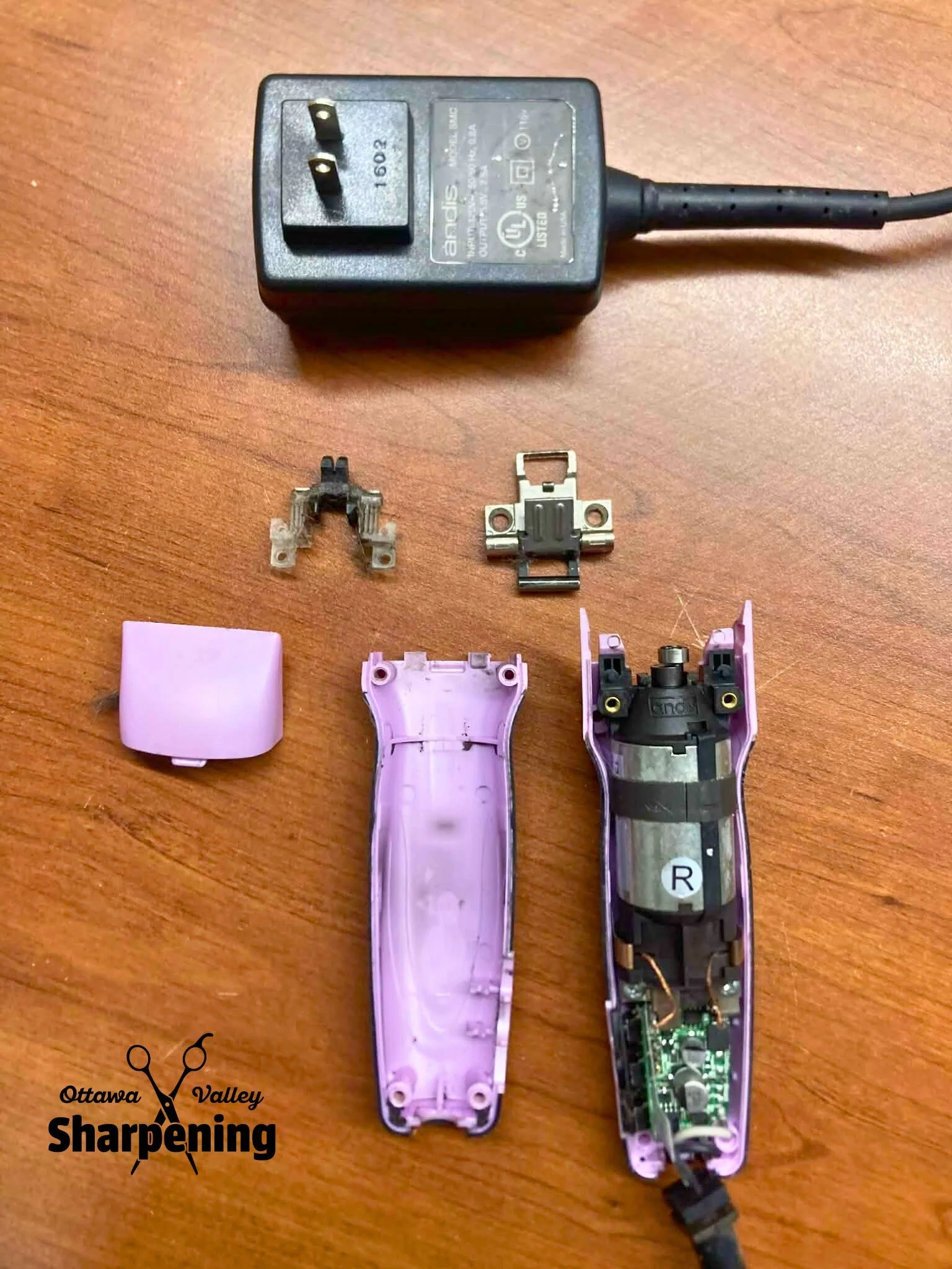 Disassembled pink electric hair trimmer with internal components on a wooden surface, including a power cord and plug.