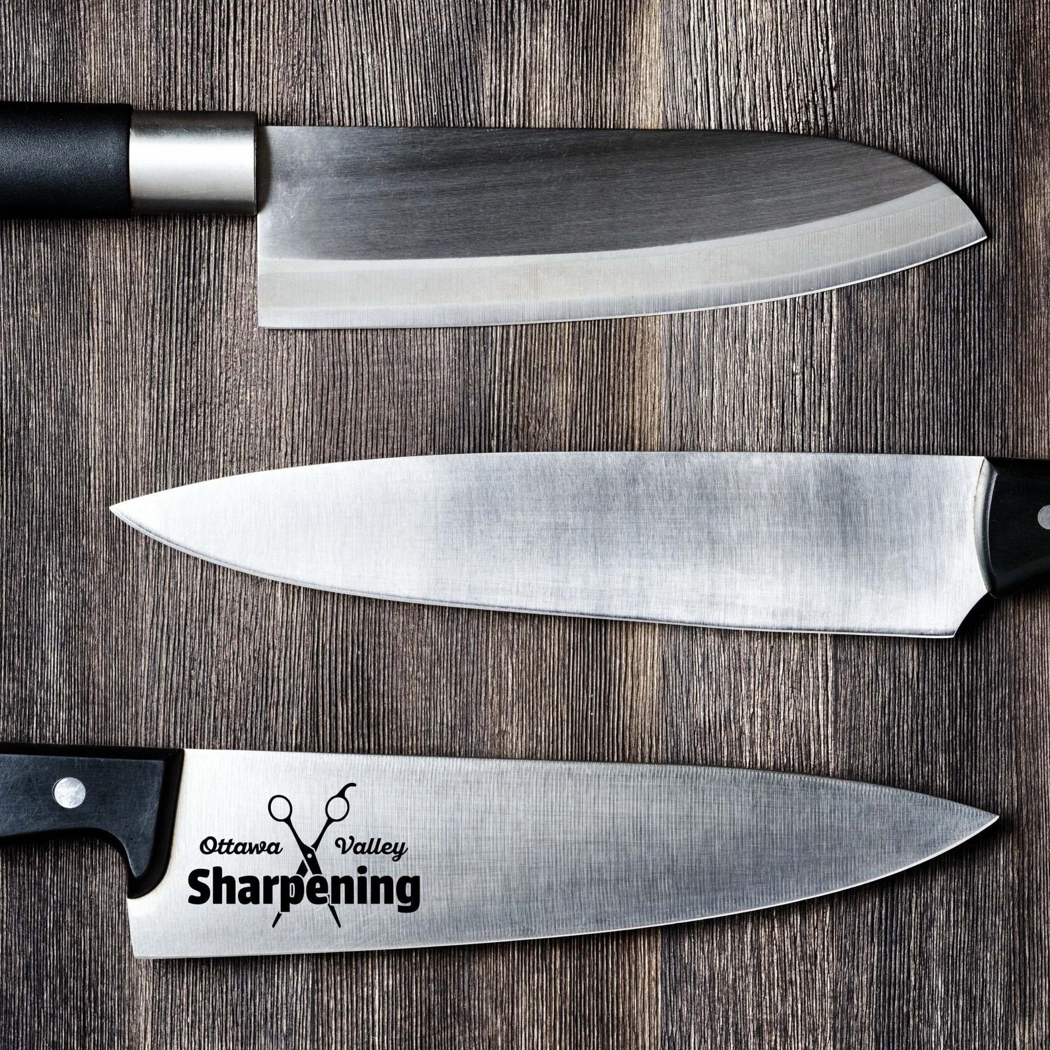 Three kitchen knives placed on a wooden surface, one with the Ottawa Valley Sharpening logo on the blade.
