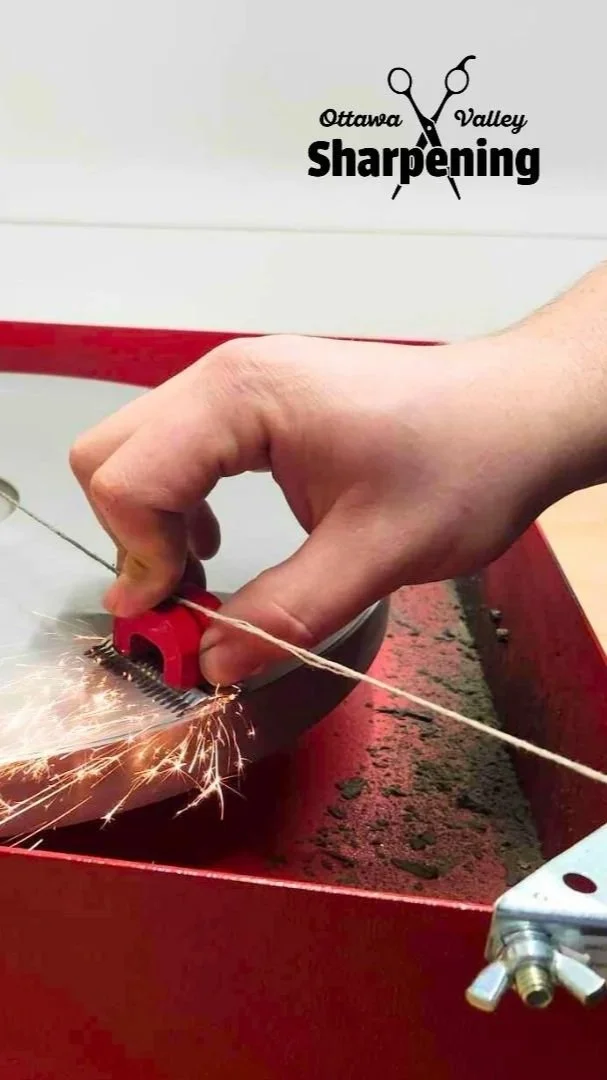A person using an angle grinder to cut a piece of metal, with sparks flying. The setting appears to be a workshop, with a red workbench and a wall with a logo reading 'Ottawa Valley Sharpening' containing scissors and razor blades.