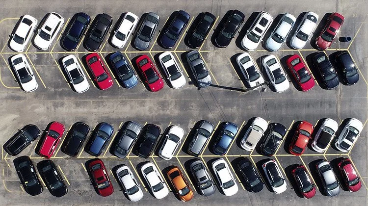 Overhead view of a parking lot filled with various parked cars arranged in organized rows.