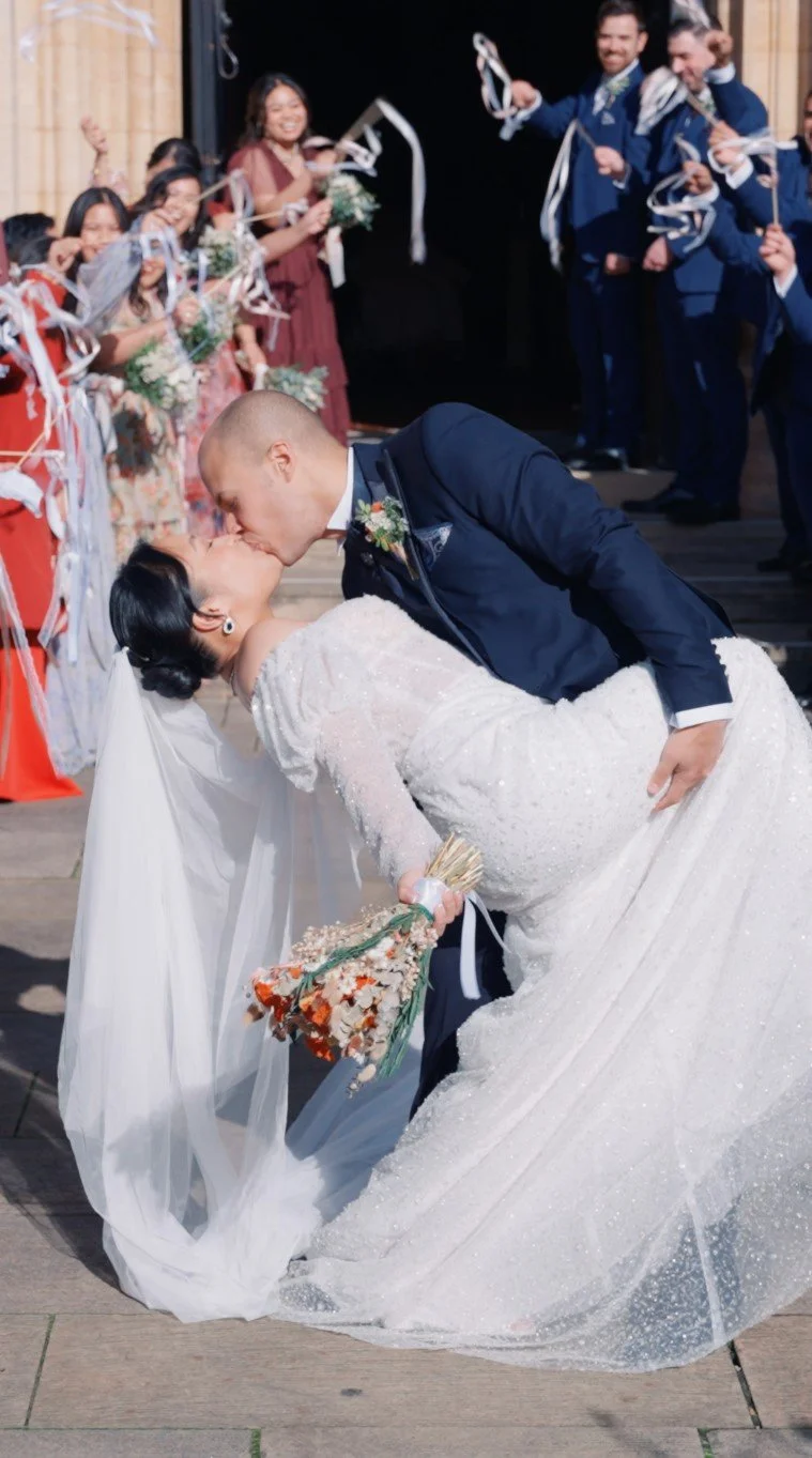 Bride and groom kissing as friends and family celebrate together on their wedding day.