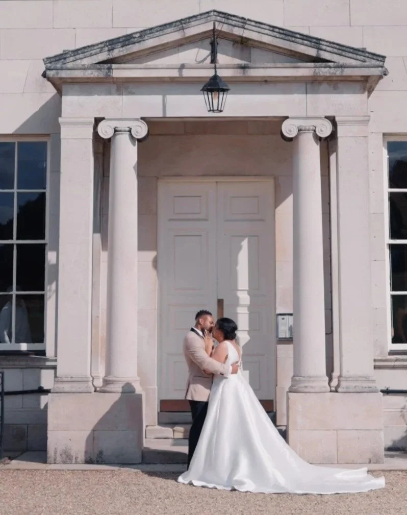 Bride and groom embracing outside a grand wedding venue, captured in a calm, natural moment.