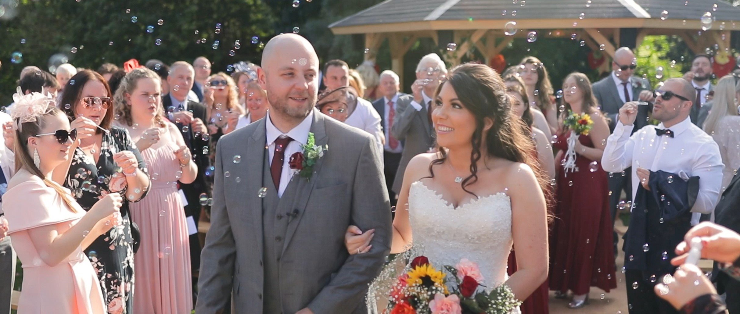A bride and groom walking arm-in-arm at their wedding surrounded by guests showering them with bubbles.
